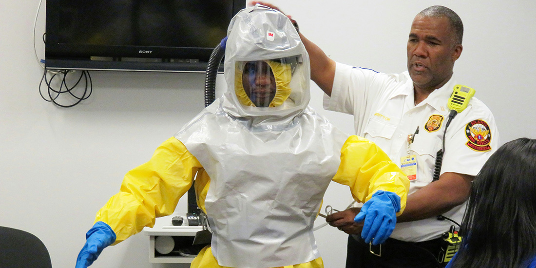 Man standing in a hazmat suite next to another man in a white officers uniform