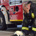 Firefighter appearing distressed sitting on side of fire truck.