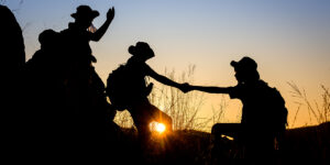silhouette of Scout students showing help to each other Hold hands and pull each other up from the cliff to explore the beautiful forest in the evening as the sun sets.